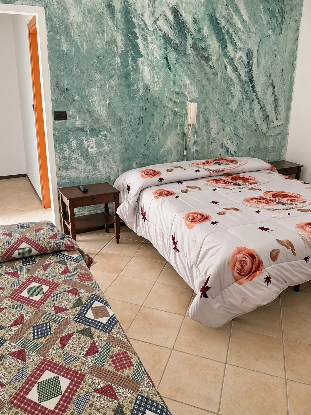 Camera col letto matrimoniale a fiori rossi, un letto singolo e la parete decorata verde