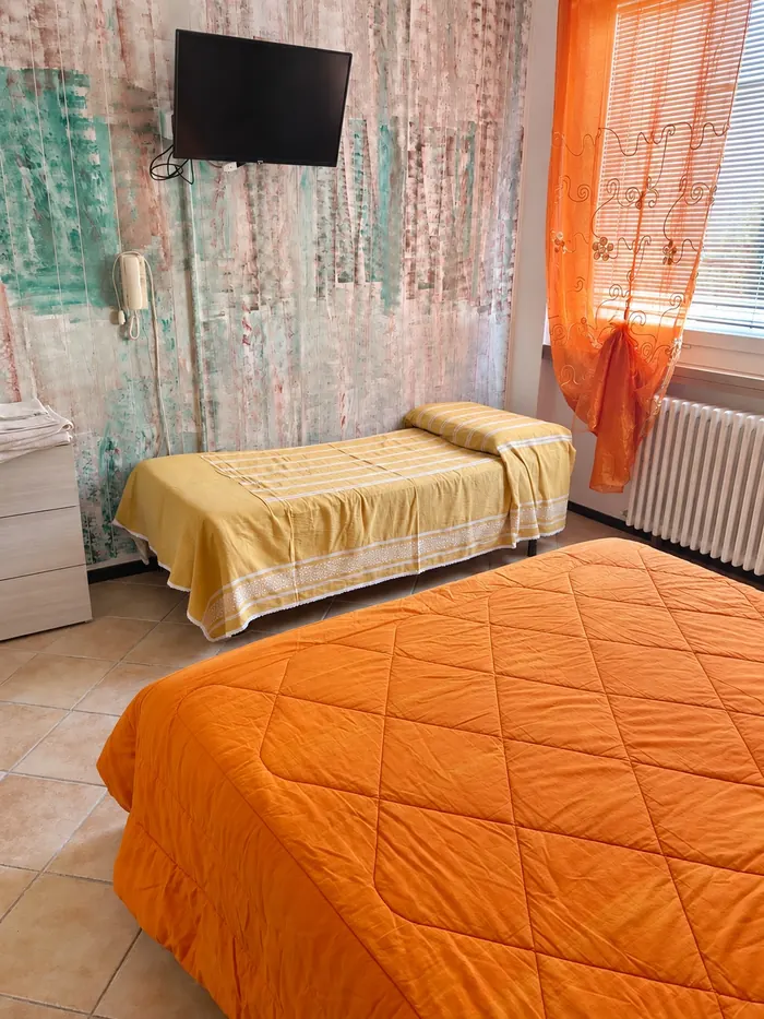 Dreibettzimmer mit orangefarbener Tagesdecke und verzierter Wand